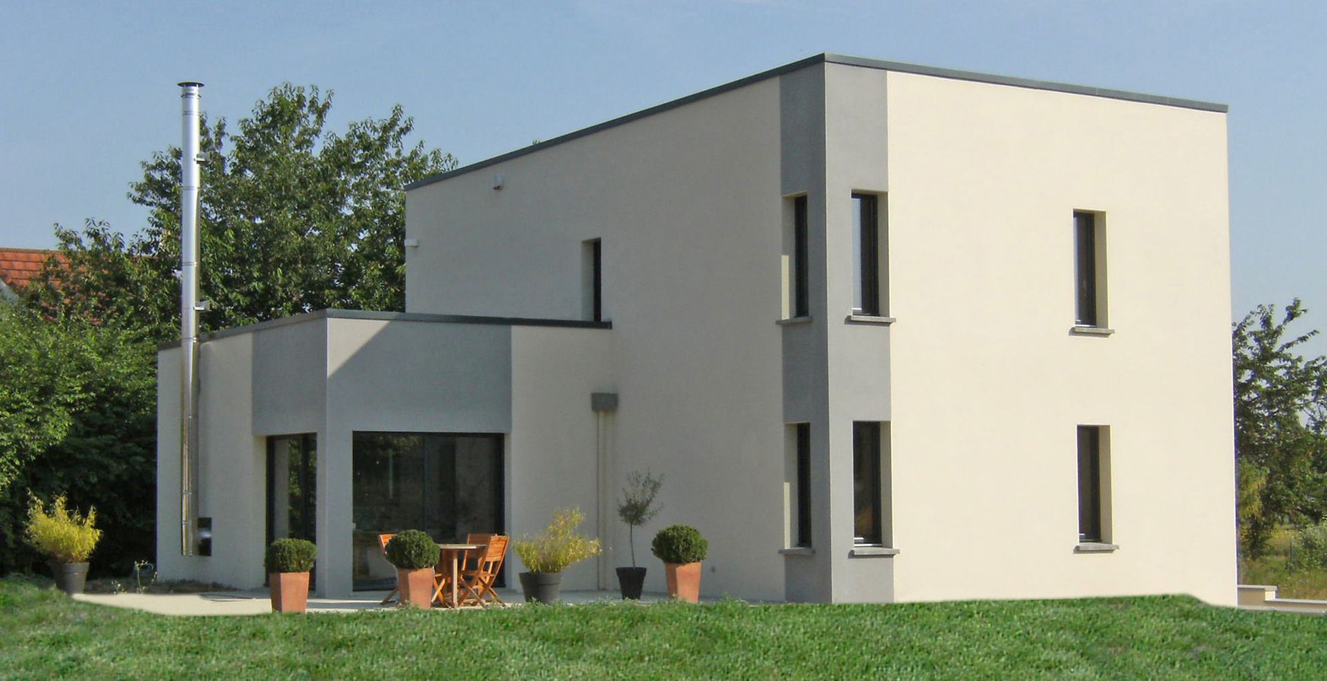 Maison moderne à deux étages avec des murs de couleur claire, des accents gris et de petites fenêtres rectangulaires.