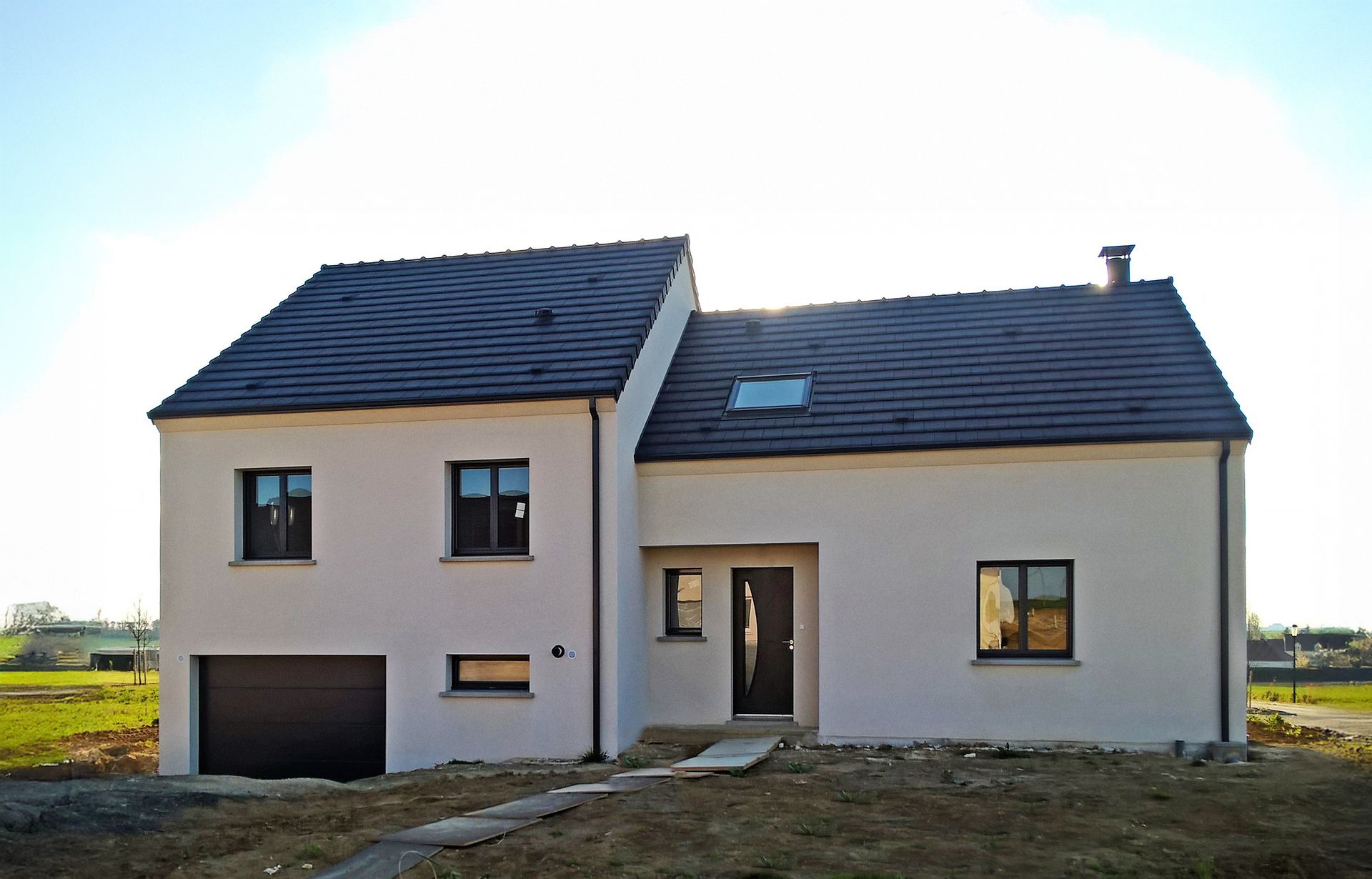 Maison moderne à deux étages avec toit noir et porte de garage marron.