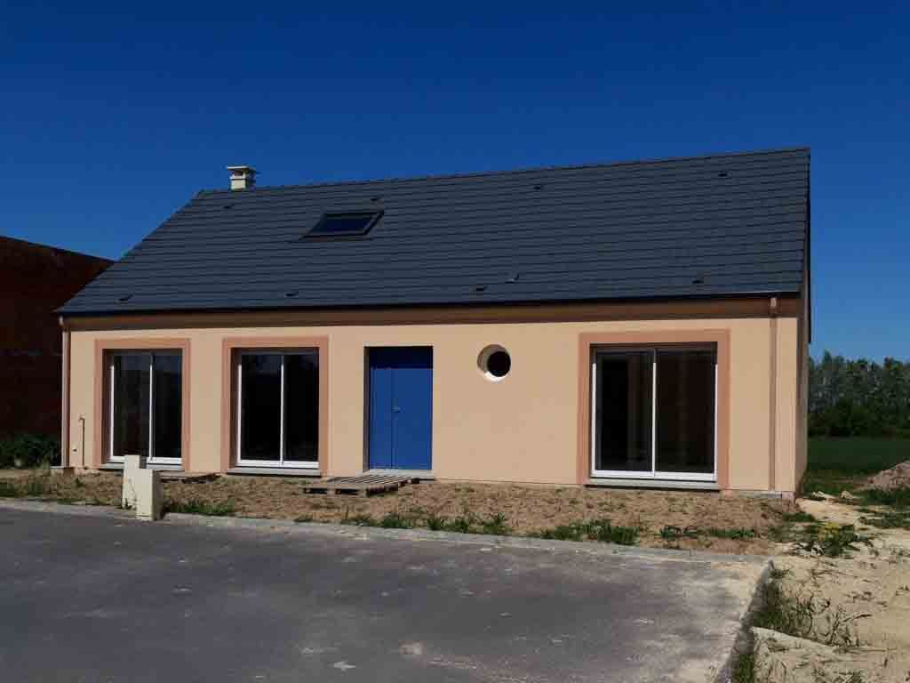 Maison beige avec porte bleue et toit gris par une journée ensoleillée.