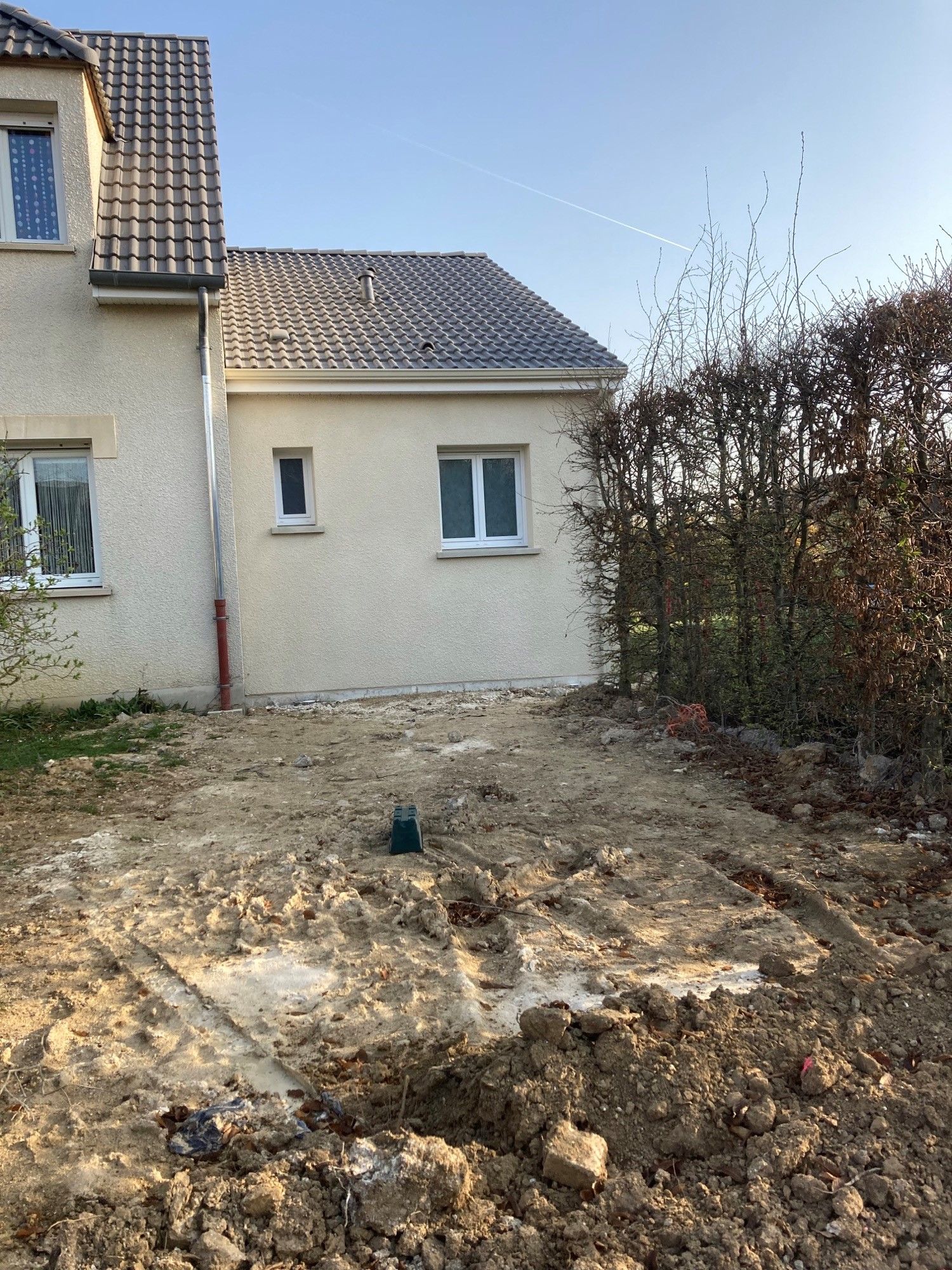 Vue latérale d'une maison beige avec un terrain dégagé au premier plan.