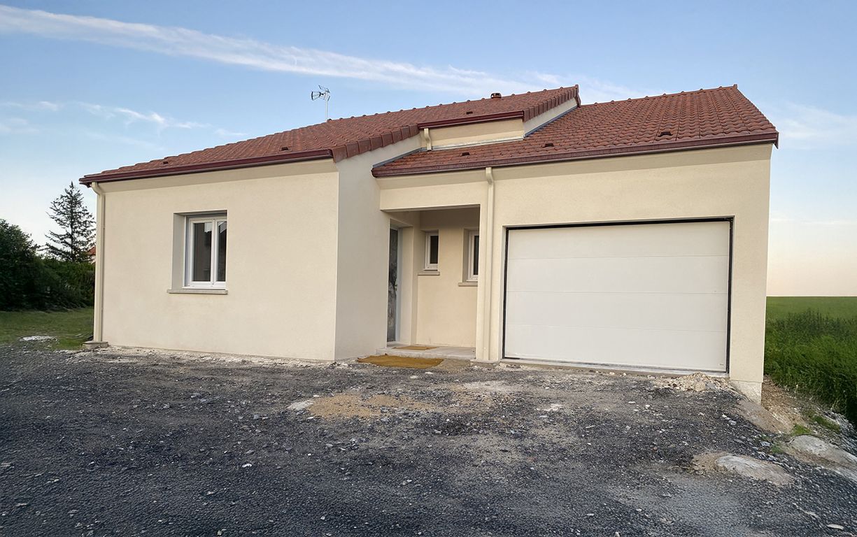 Maison beige avec toit en tuiles rouges, porte de garage blanche et cour en gravier contre un ciel bleu.
