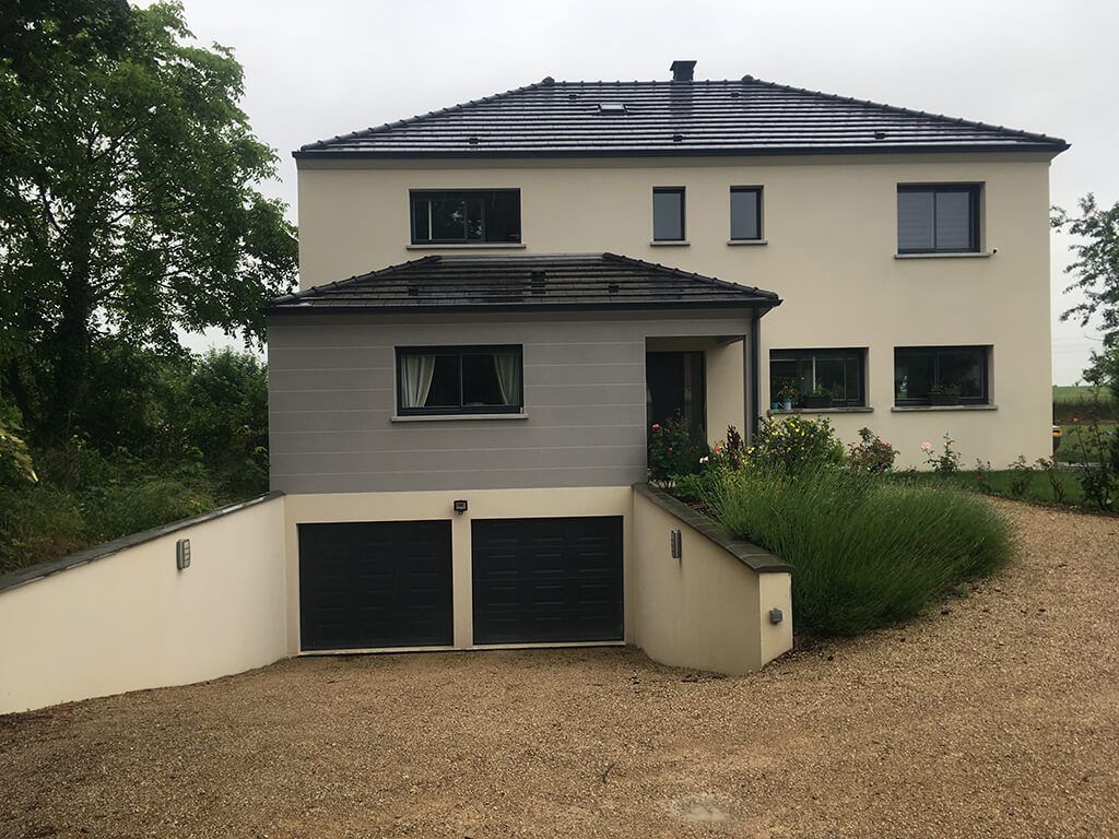 Maison beige à deux étages avec garage gris, allée et aménagement paysager vert.
