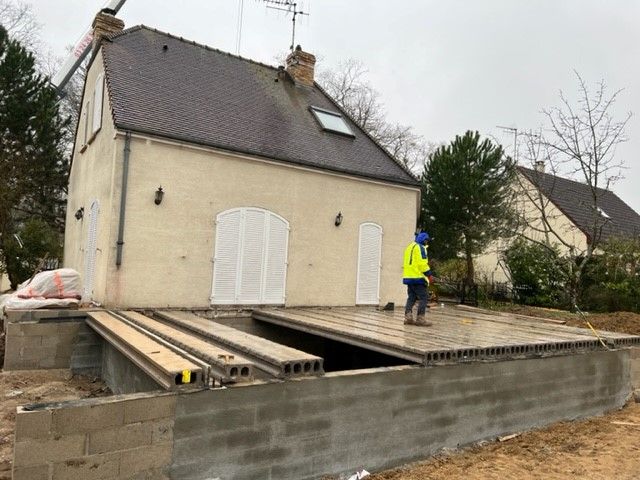Une maison avec une terrasse partiellement construite, une personne en équipement de sécurité se tient dessus.