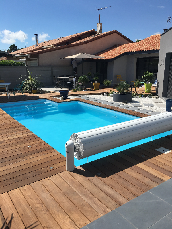 Terrasse bardée en bois autour d'une piscine bleue
