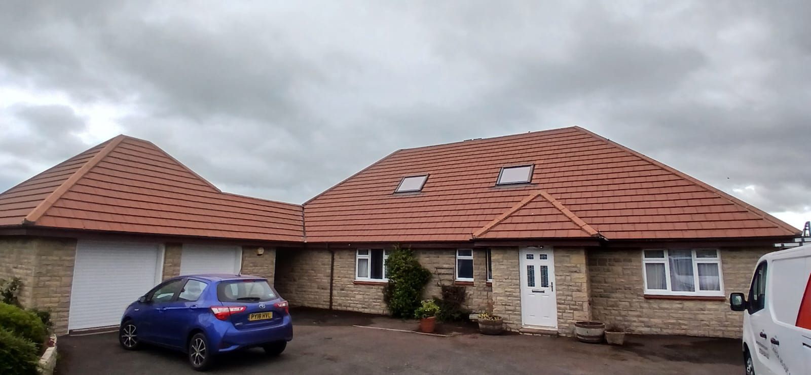 Single-story house with red tiled roof and blue car parked in front under a cloudy sky