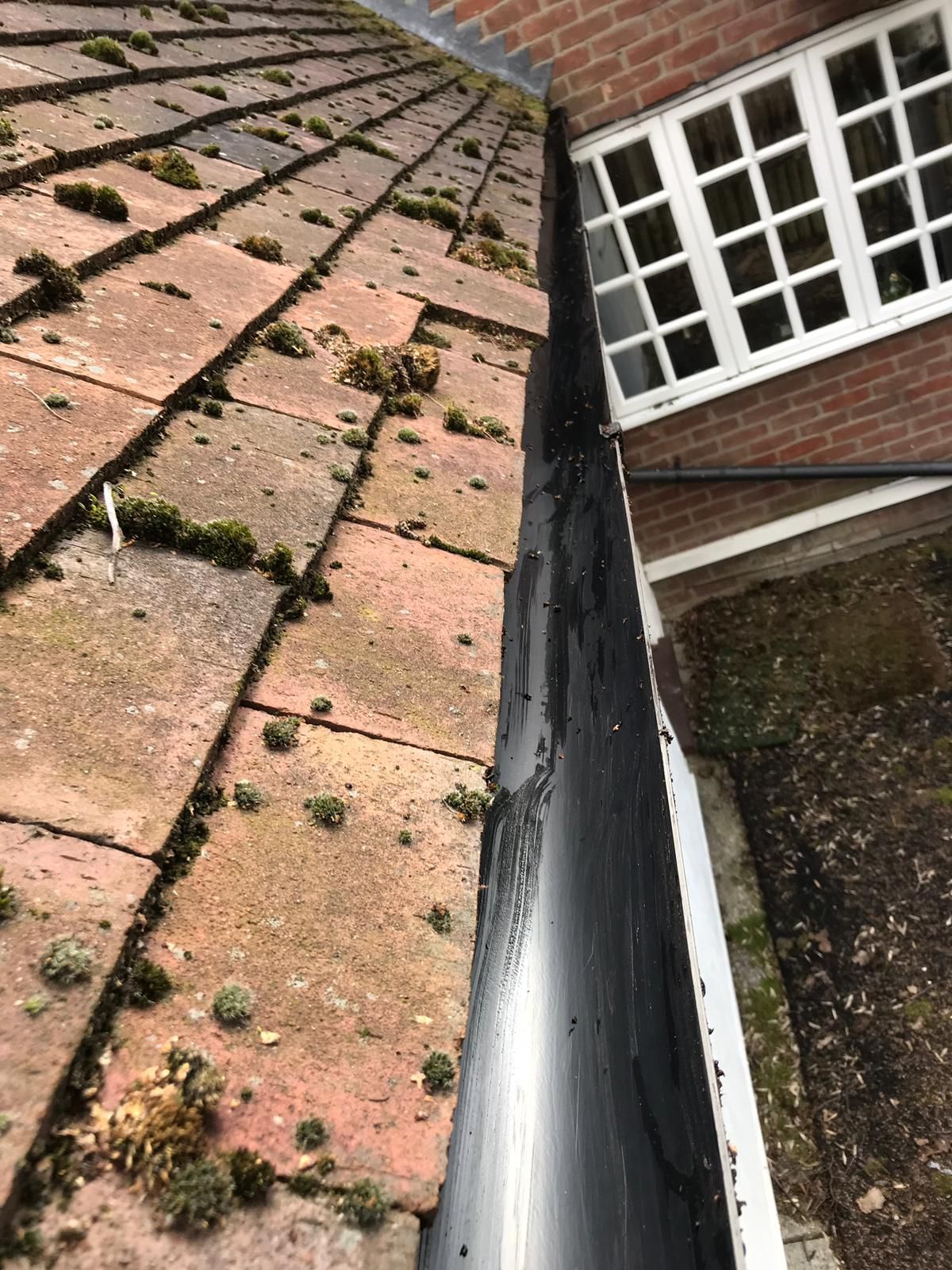 Damaged roof with missing tiles, moss growth, and a gutter beside a brick house window