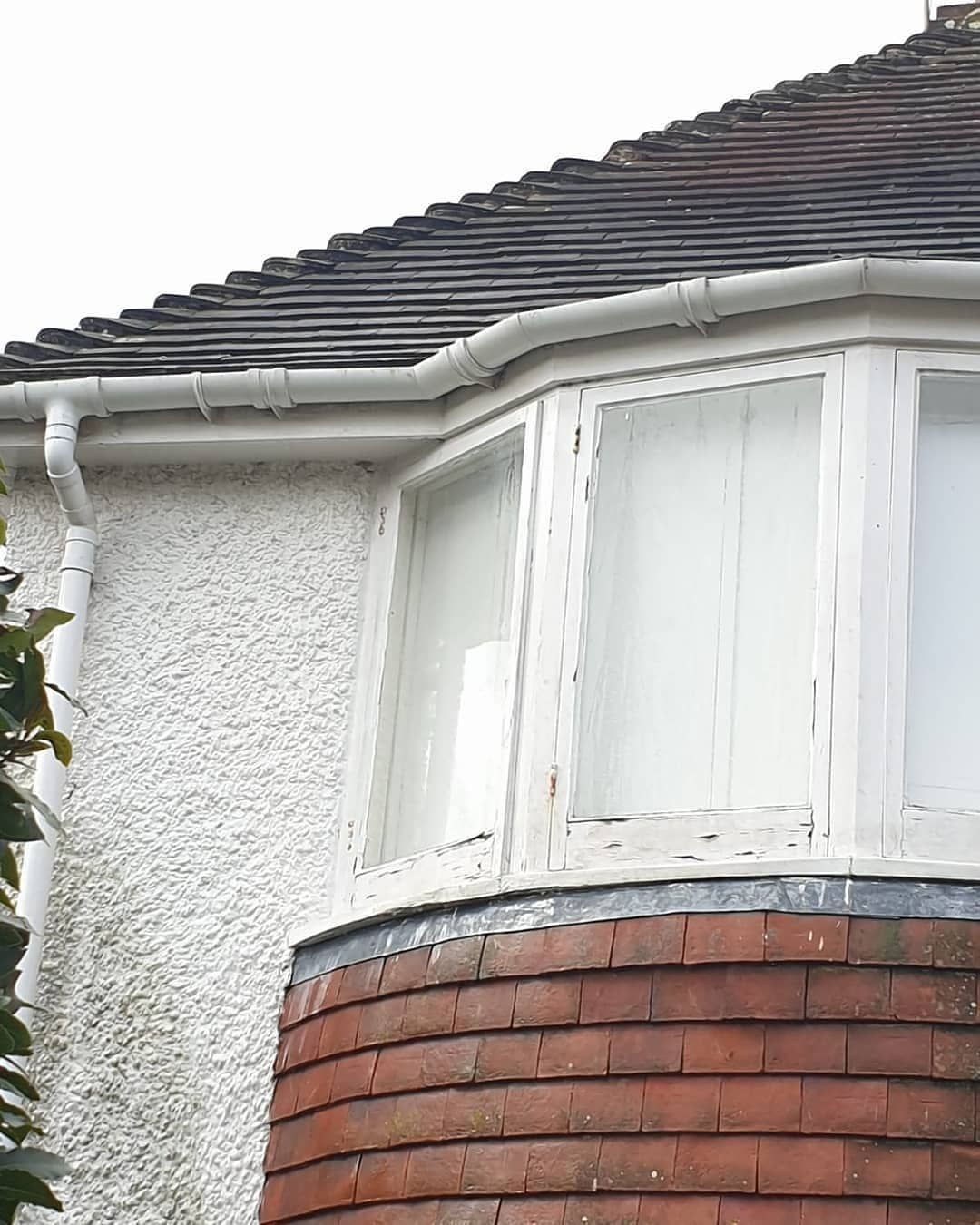 White bay window on a gray house with a brick base and dark tiled roof