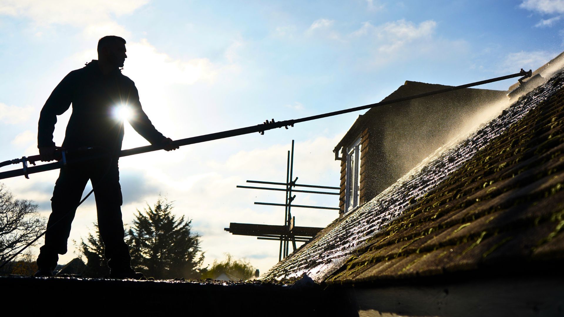Worker with a power washer cleaning a roof in bright sunlight