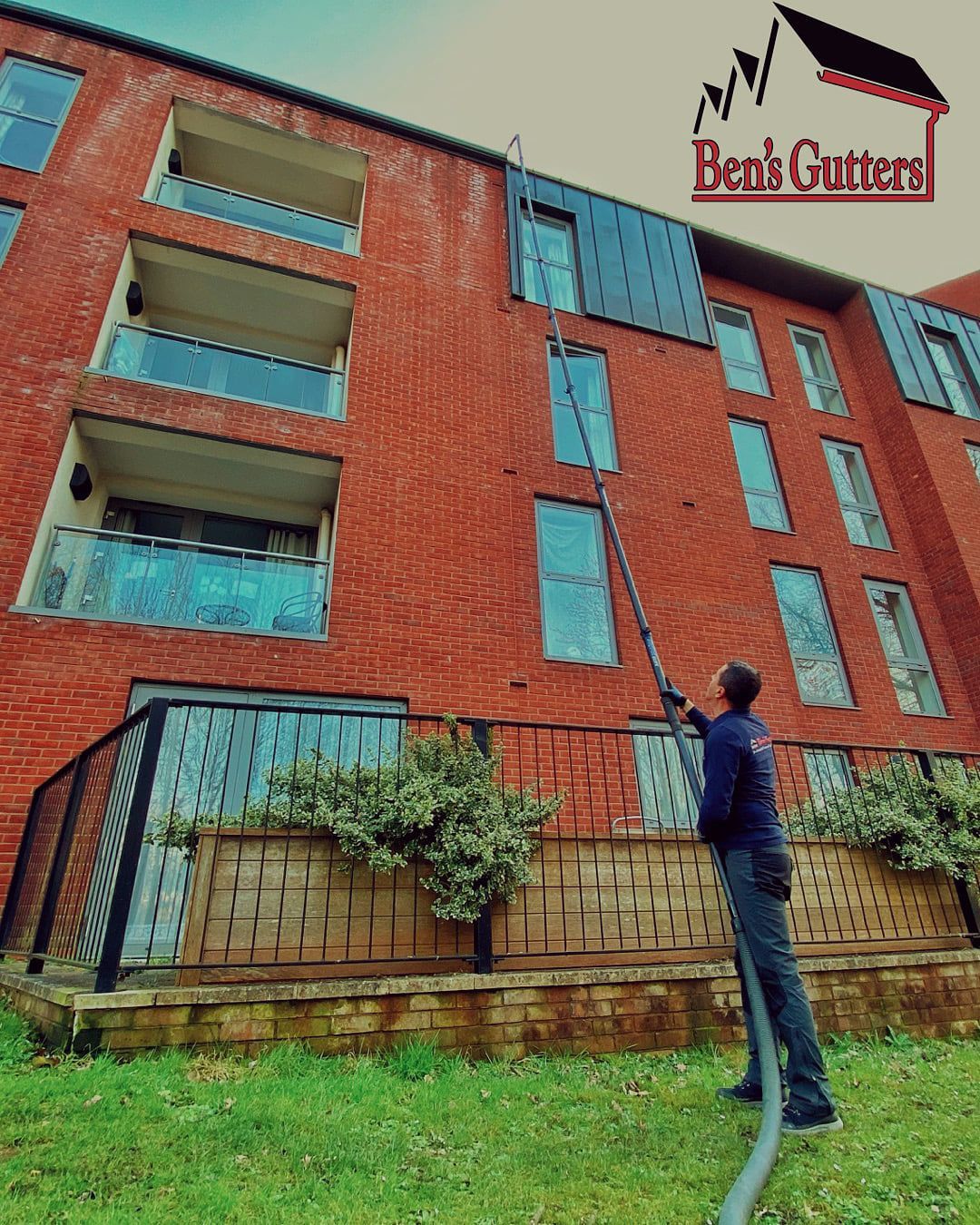 Red brick apartment building with blue windows and a person standing on the grass below