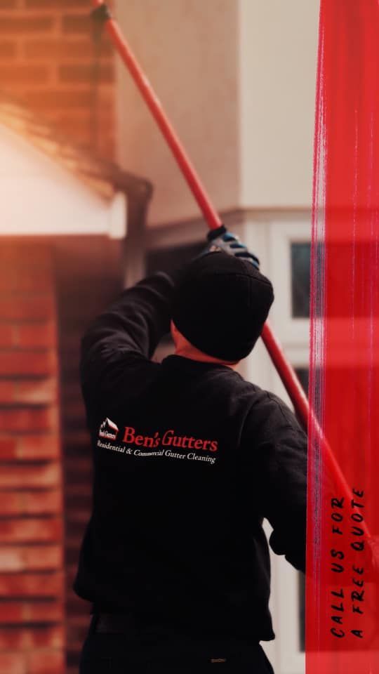 Person in a black hoodie painting a building exterior with a long-handled roller near red trim.