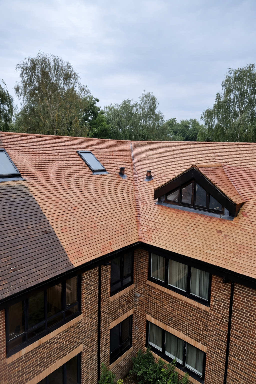 Aerial view of a red-tiled apartment building roof with skylights and trees in the background