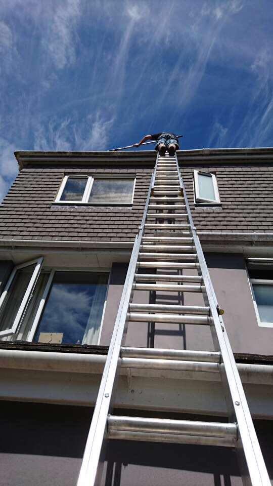 Person on ladder cleaning roof gutter against a blue sky.