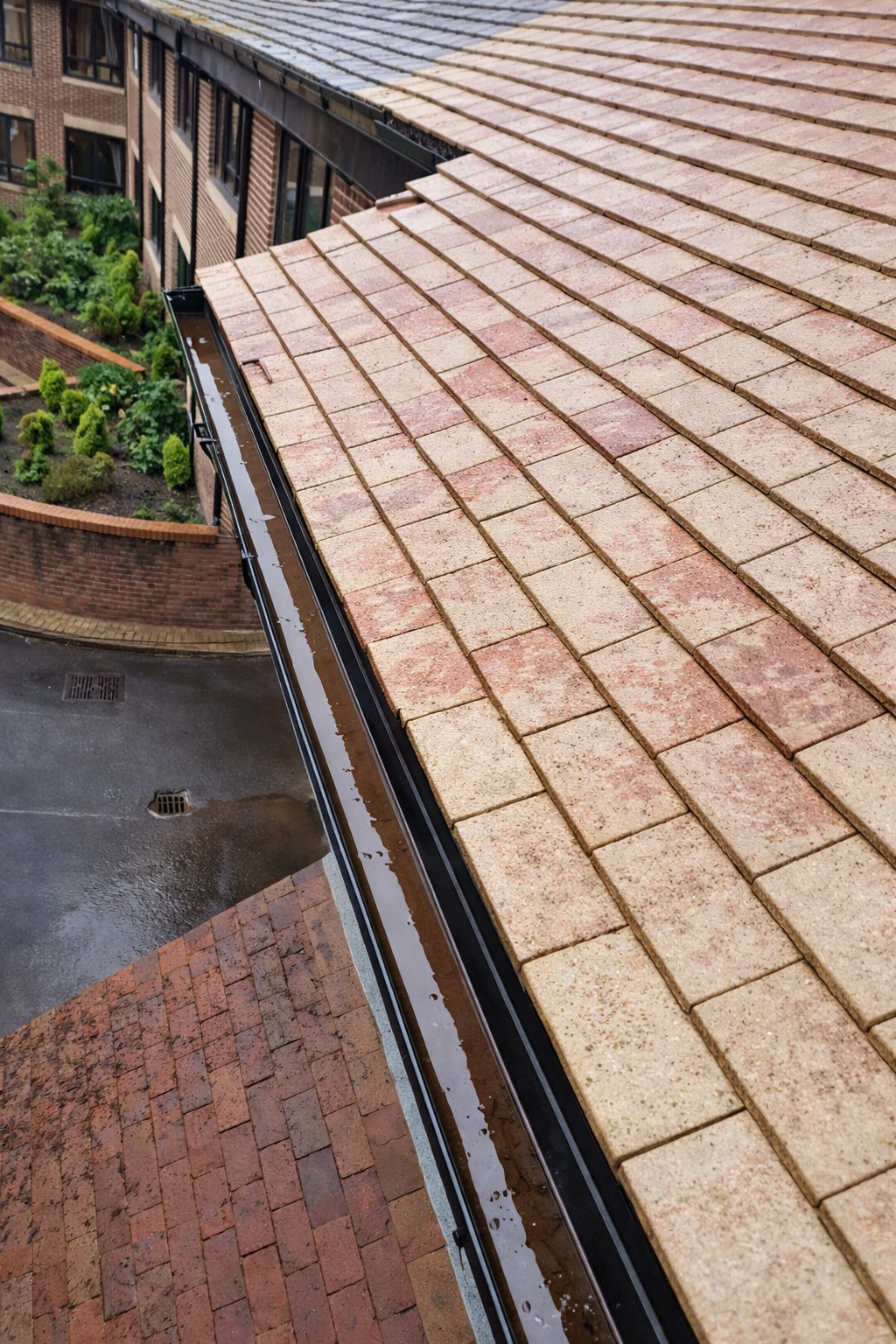 Rainy rooftop with tan tiles beside a brick courtyard and curved building wall