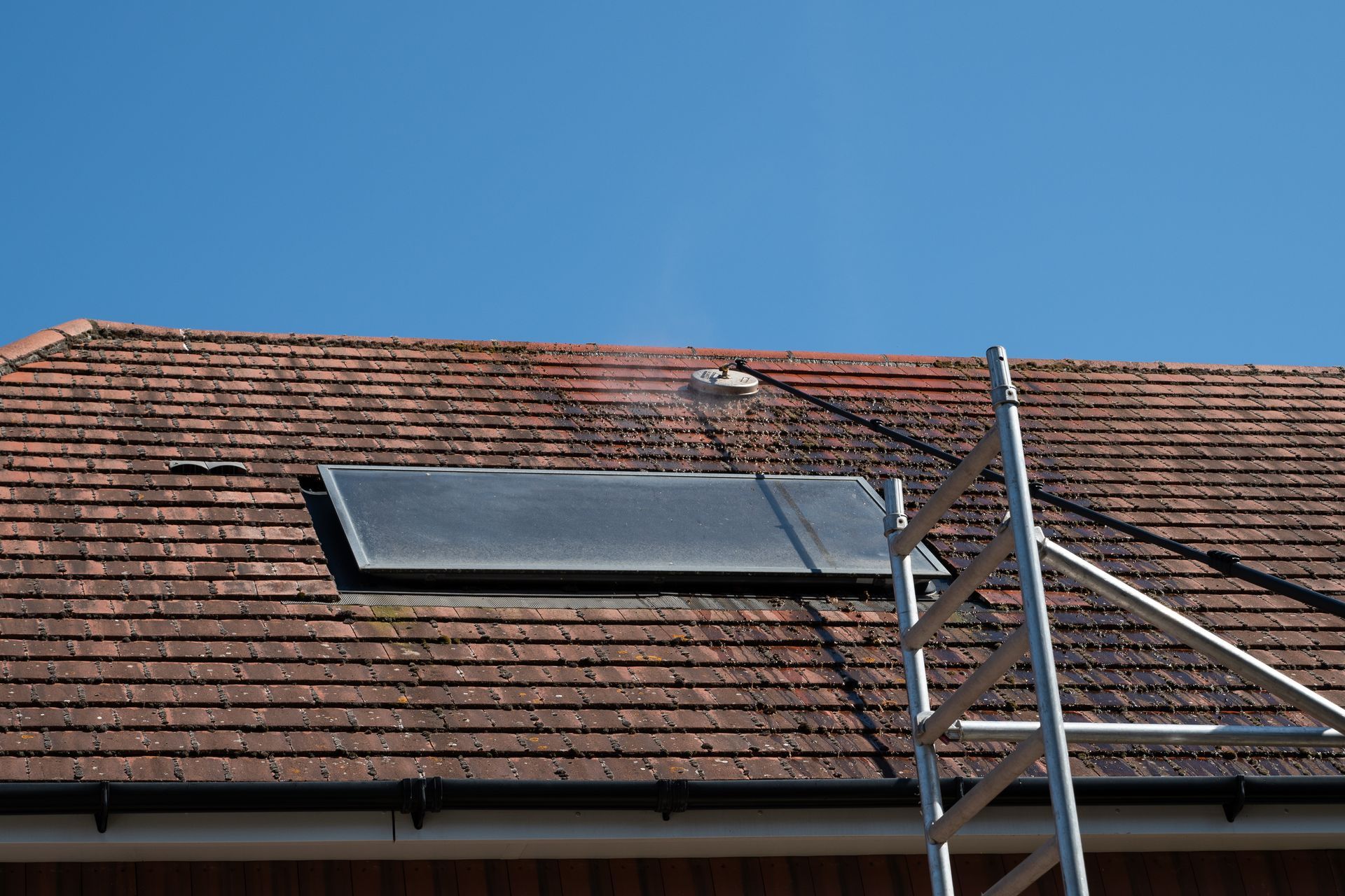 Roof with solar panel and chimney under a blue sky, with a metal ladder in the foreground