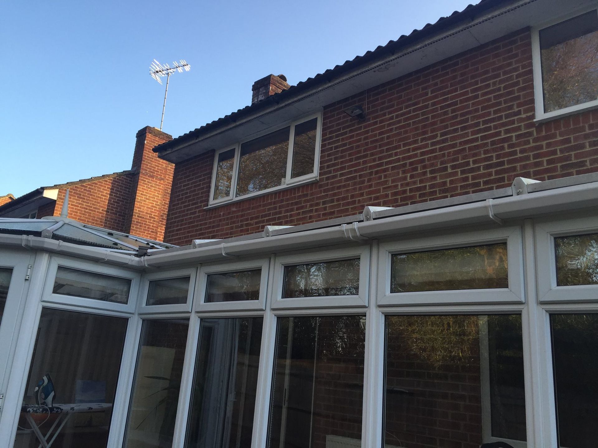 Brick house exterior with white conservatory and windows under a blue sky