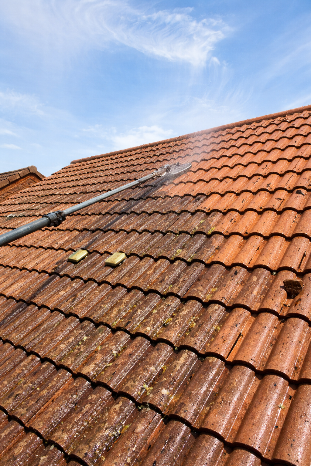 Wet terracotta tile roof with a long roof ladder under a blue sky