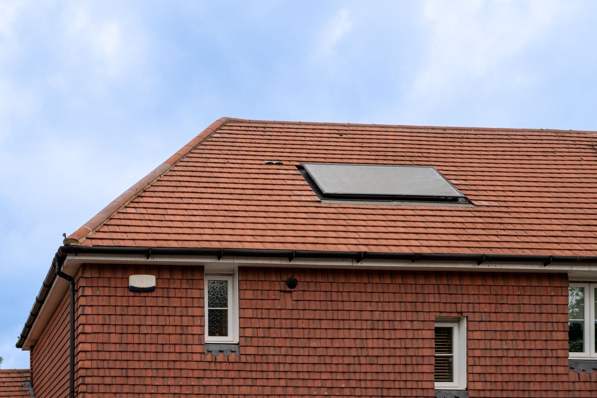 Red-tiled house roof with a solar panel under a blue sky