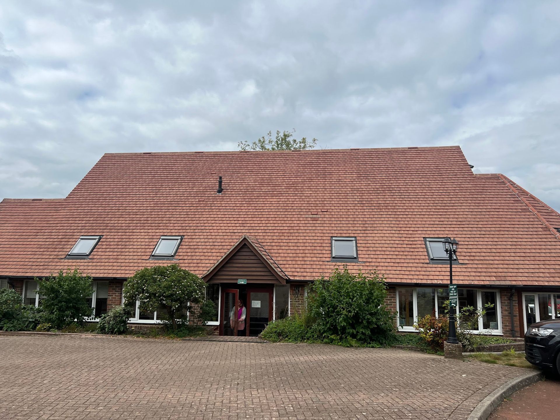 Red-roofed building with dormer windows and a central entrance under a cloudy sky