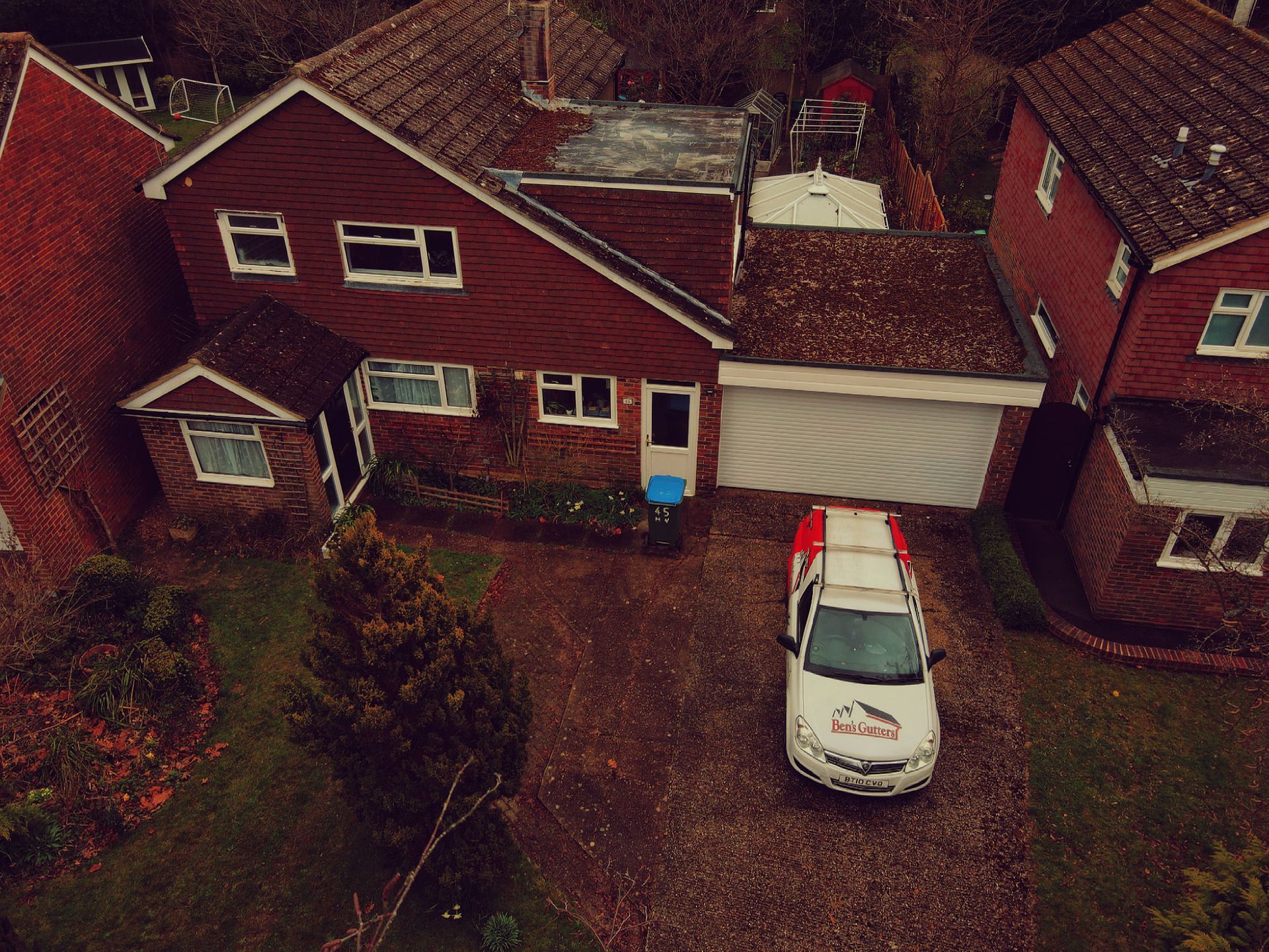 Aerial view of a red brick house with a white garage and a car parked in the driveway.
