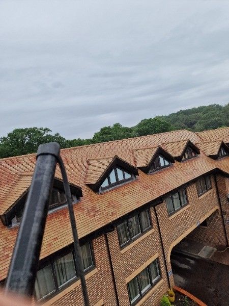 Tilted view of brick building with red roof and dormer windows under a cloudy sky