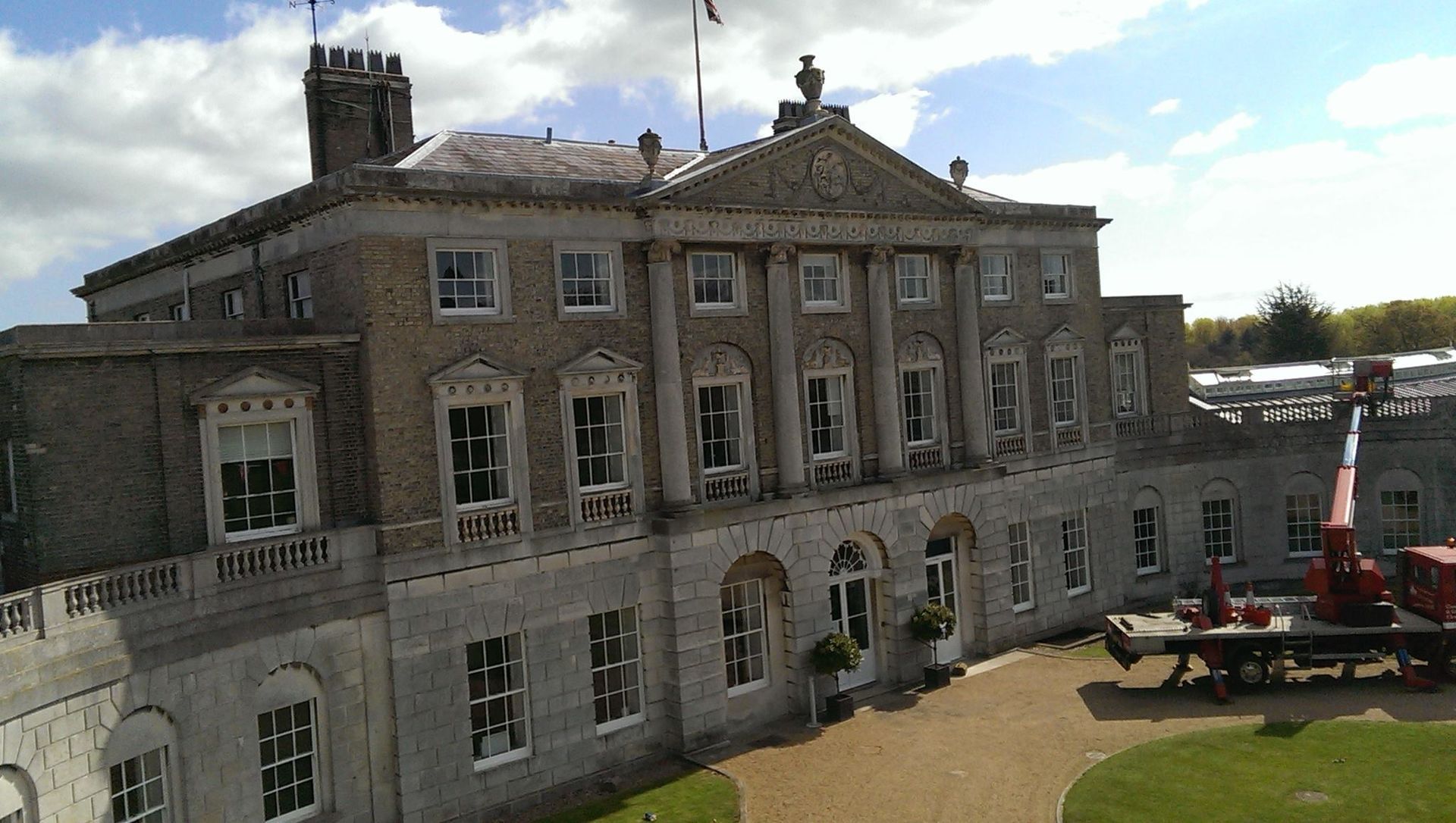 Stone mansion with many windows and a crane in front, under a partly cloudy sky