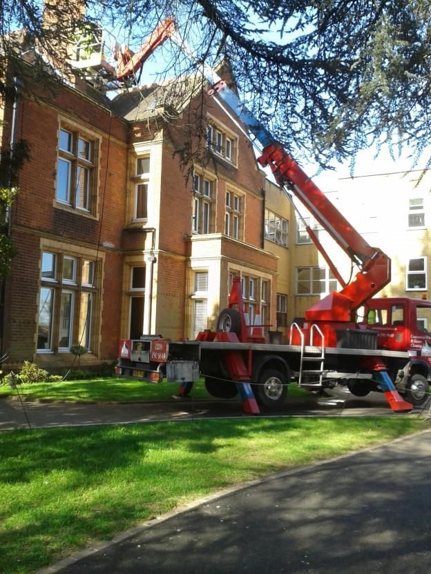 Red crane truck parked beside a brick building, with a large ladder extended overhead.