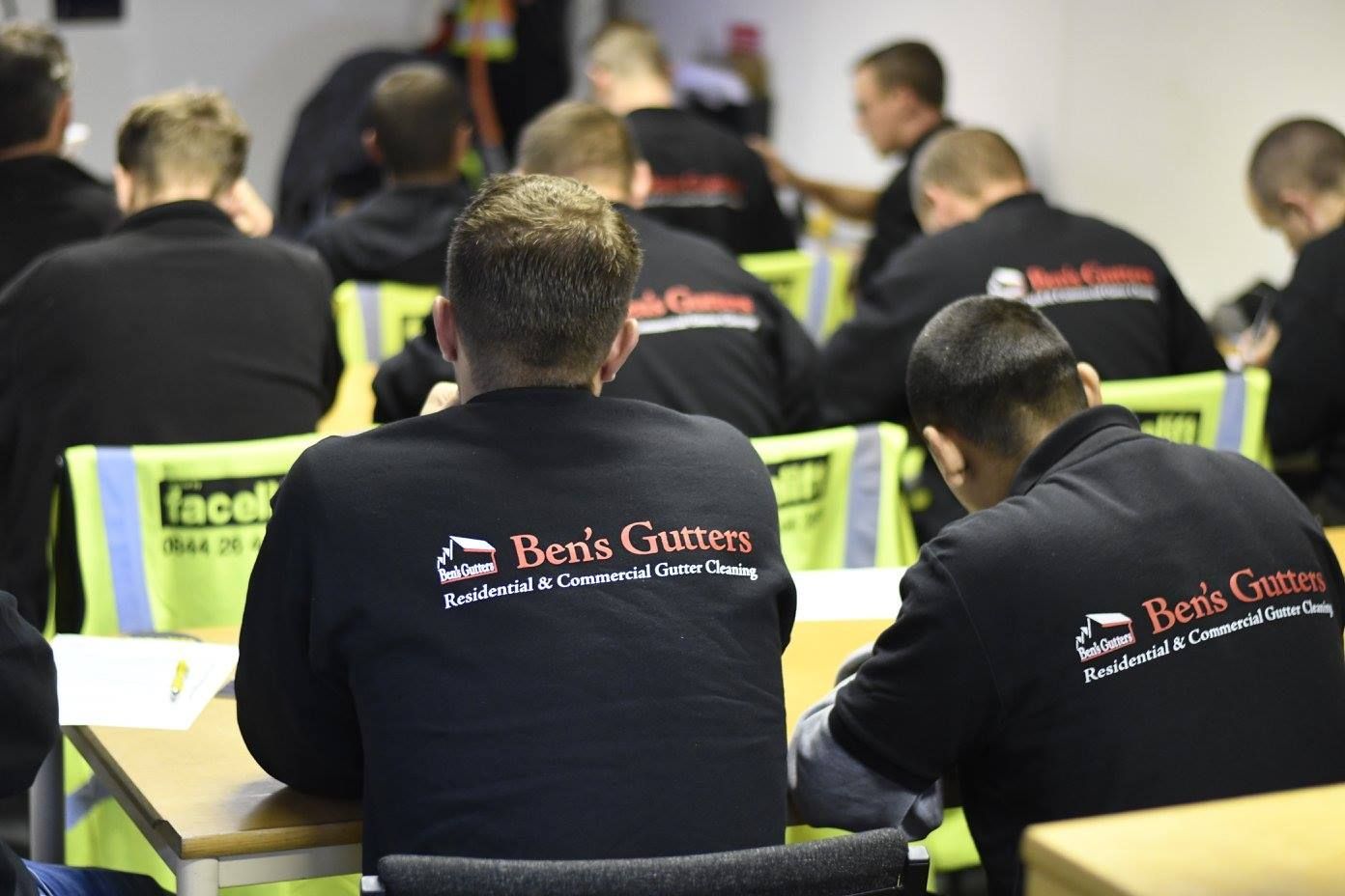Workers in black jackets with red logos seated at desks in a training room