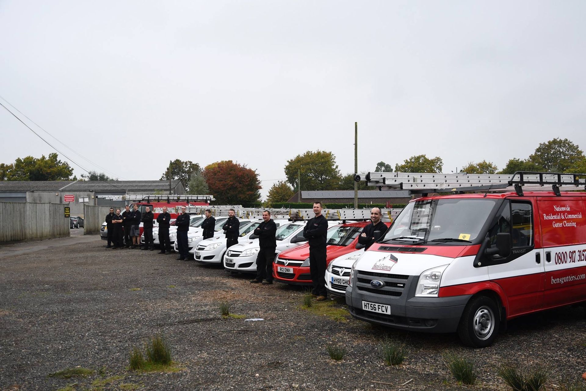 Row of red and white emergency vans parked on a gravel lot under an overcast sky