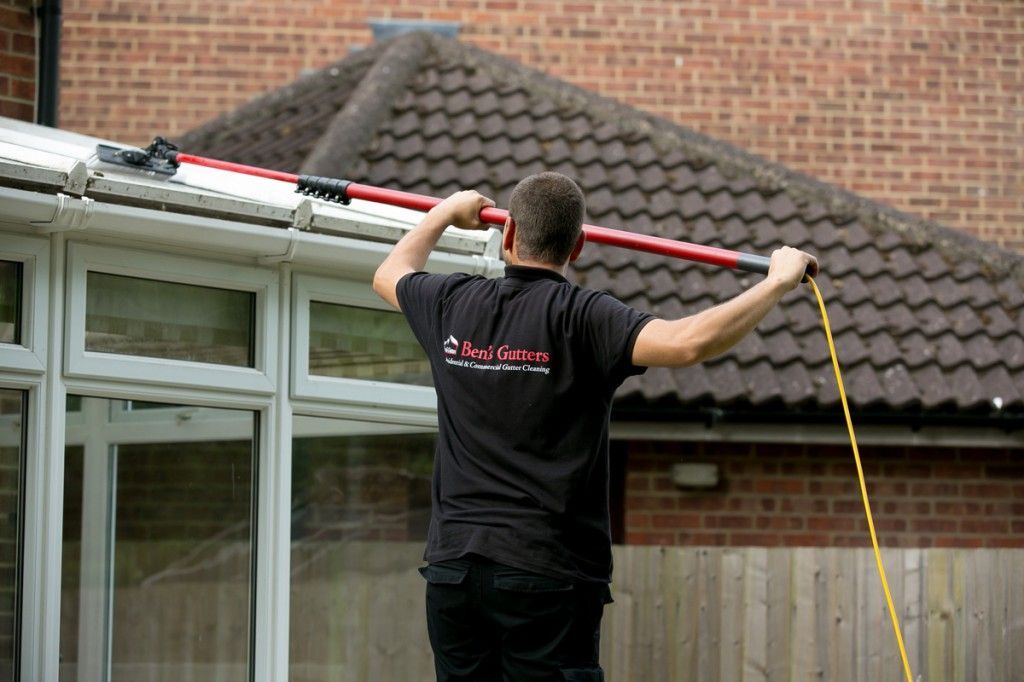 Person using a long pole tool to clean gutters on a house roof.