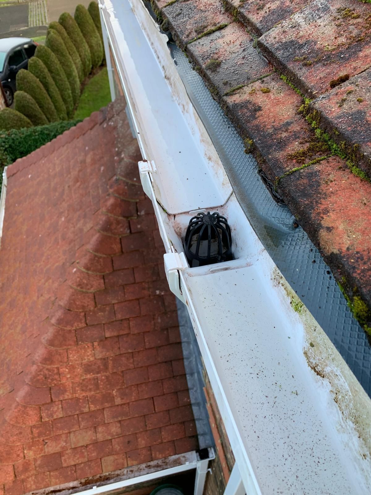 Damaged white gutter beside red-tiled roof, with a black object lodged inside it.