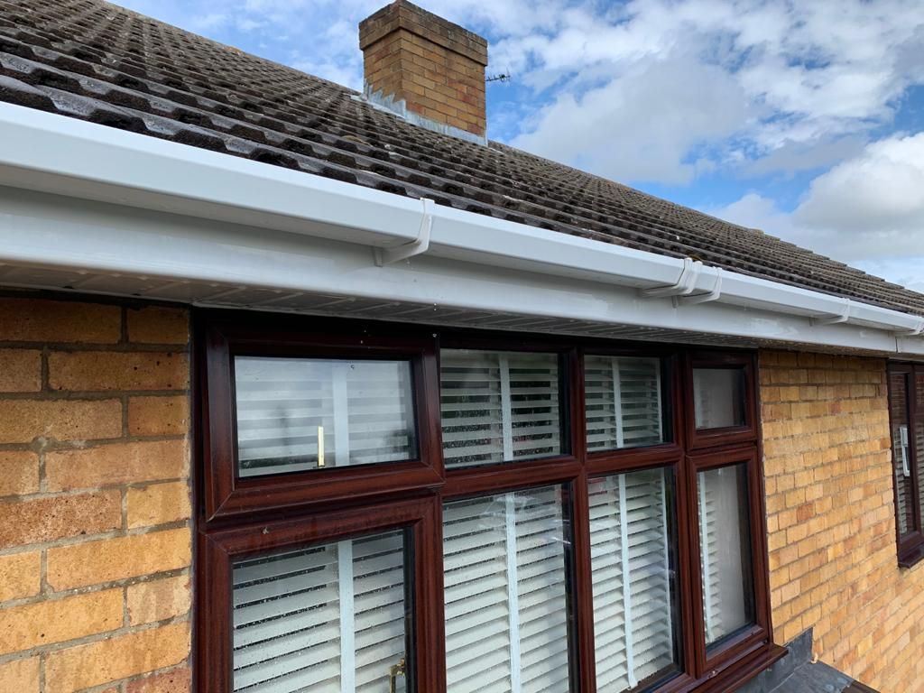 Close-up of a brick house window with white blinds under a tiled roof and cloudy sky