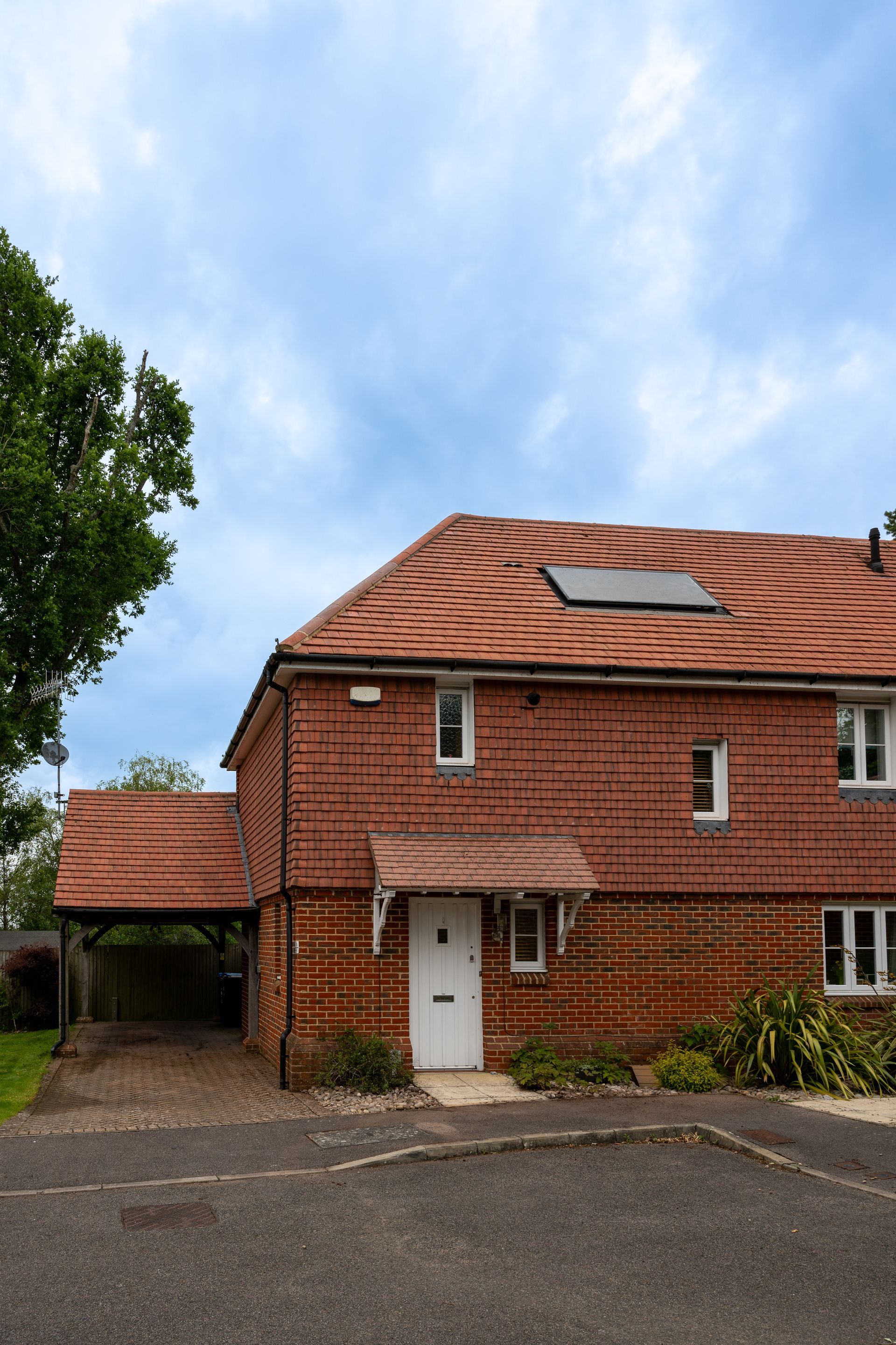 Brick house with red roof, skylight, white door, and a driveway under a partly cloudy sky