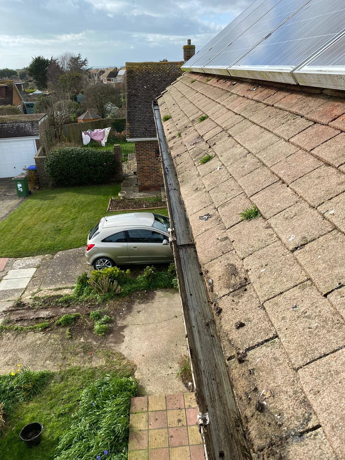 Rooftop view of a sloped tiled roof beside a driveway, lawn, and parked silver car