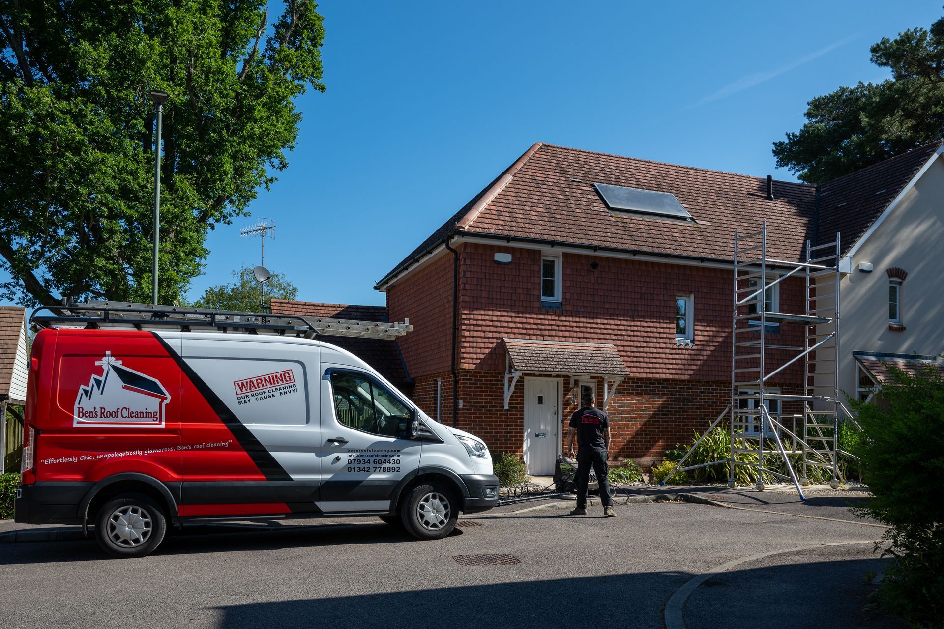 Delivery van parked outside a brick house with two workers and construction materials in the yard