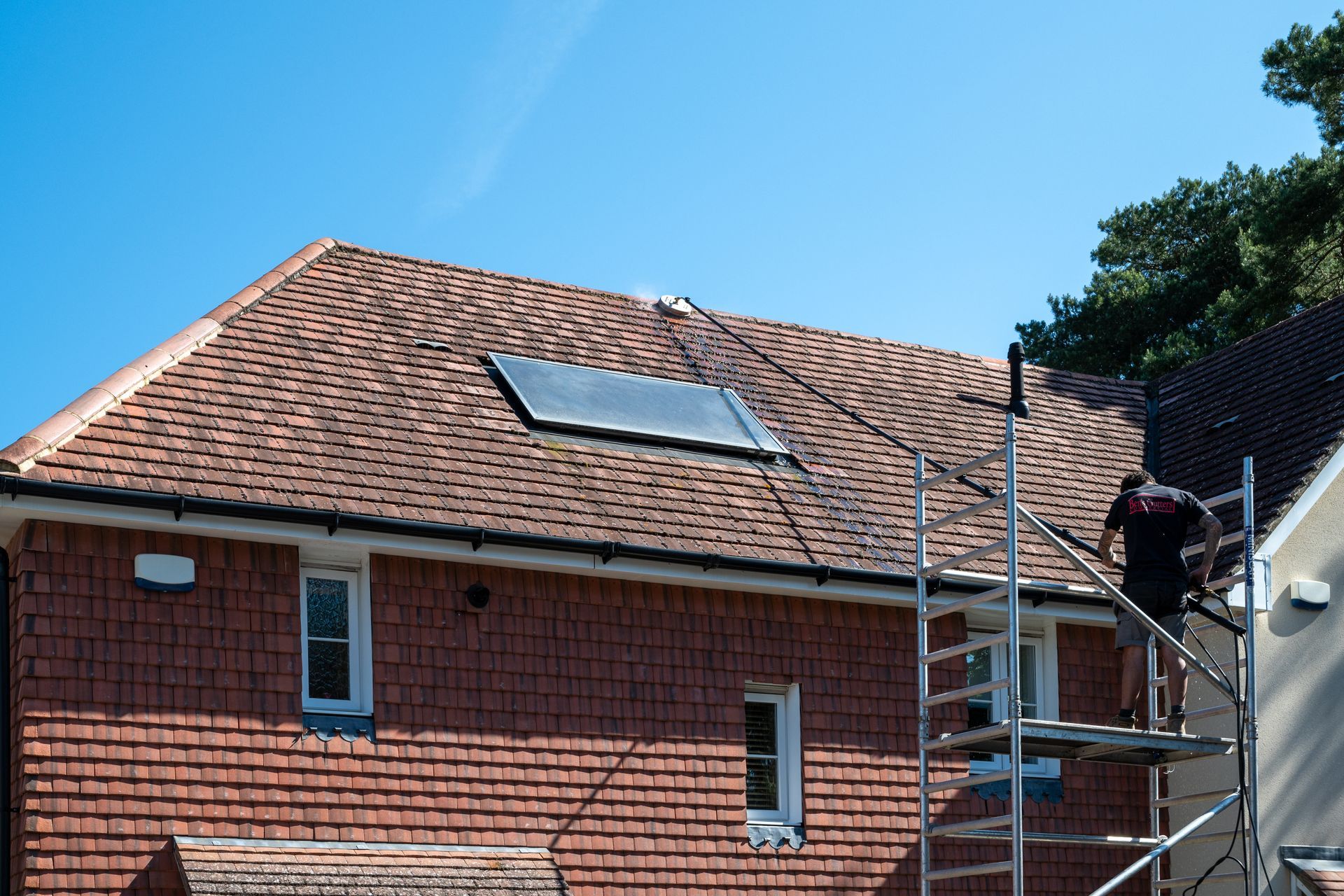 Red-tiled roof with a solar panel and scaffolding on a brick house under a blue sky