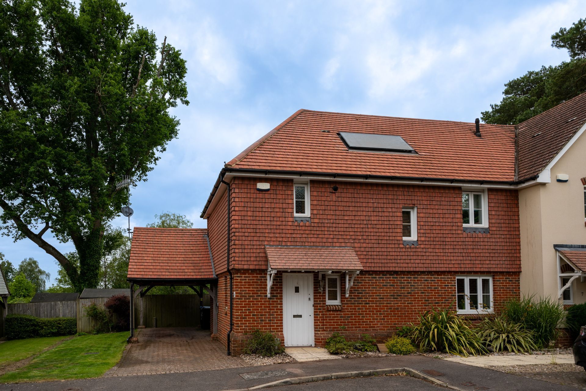 Red-brick suburban house with a tiled roof, driveway, and carport beneath a cloudy sky