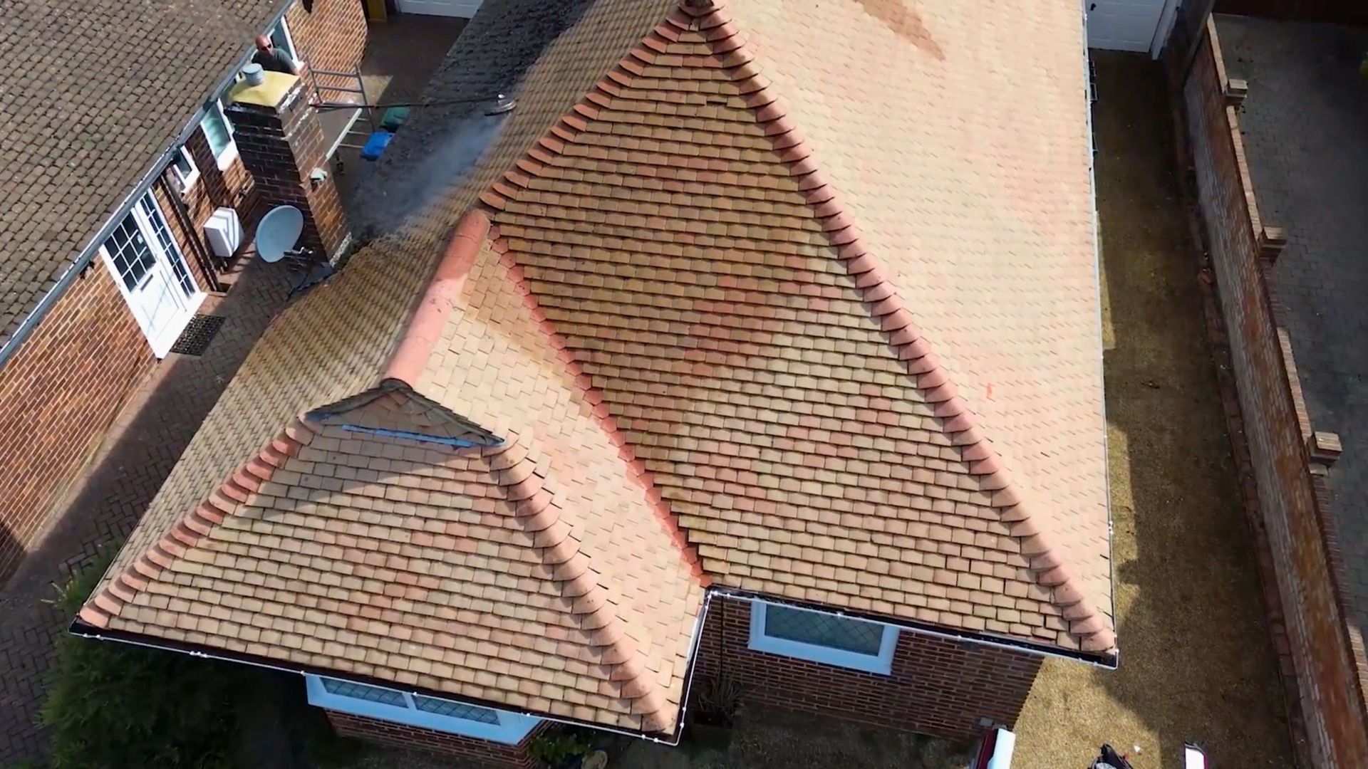 Aerial view of a house with red-tiled roofs and blue-trimmed windows beside neighboring buildings.