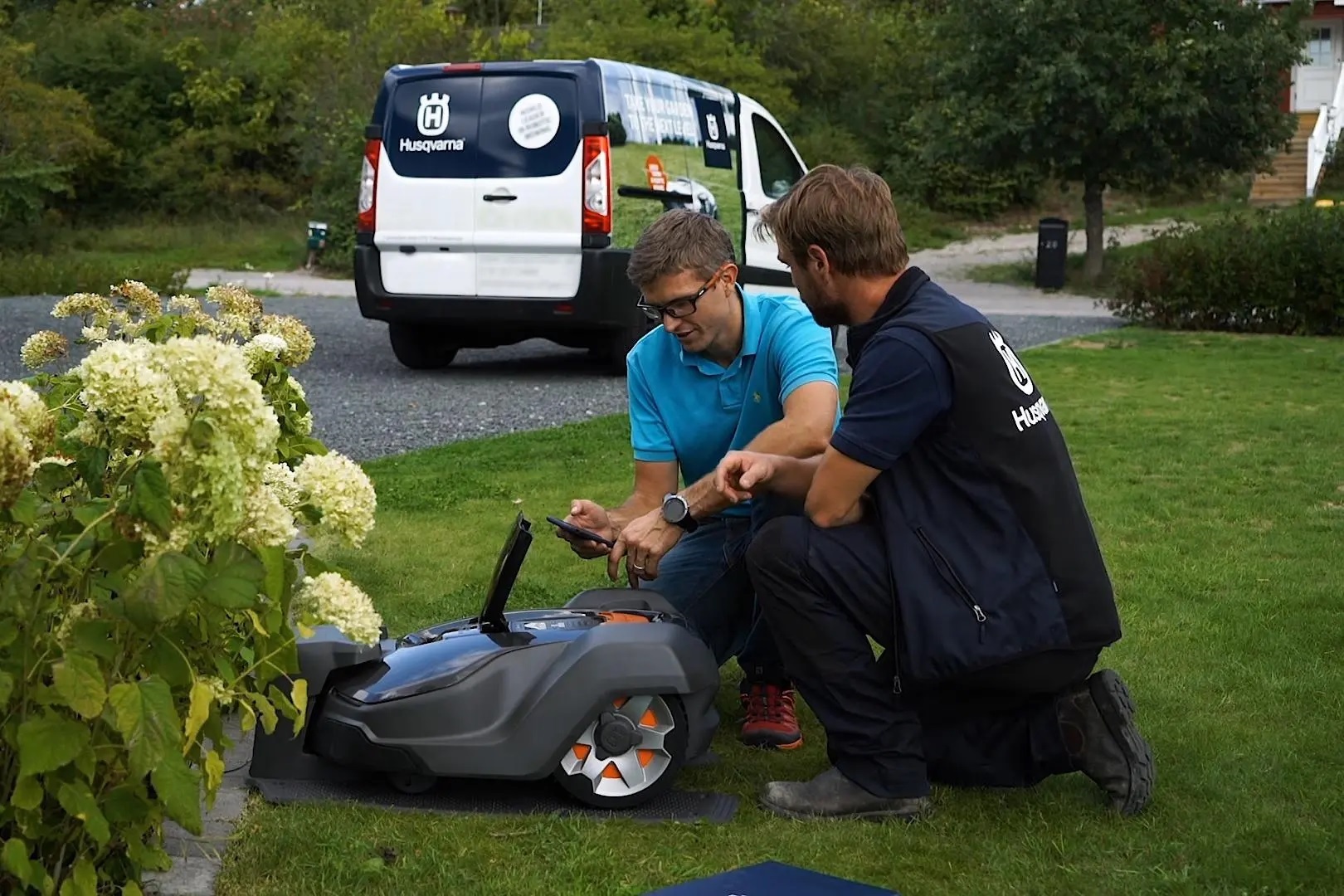 Ein Husqvarna Mähroboter fährt neben einem Baum vorbei über den Rasen