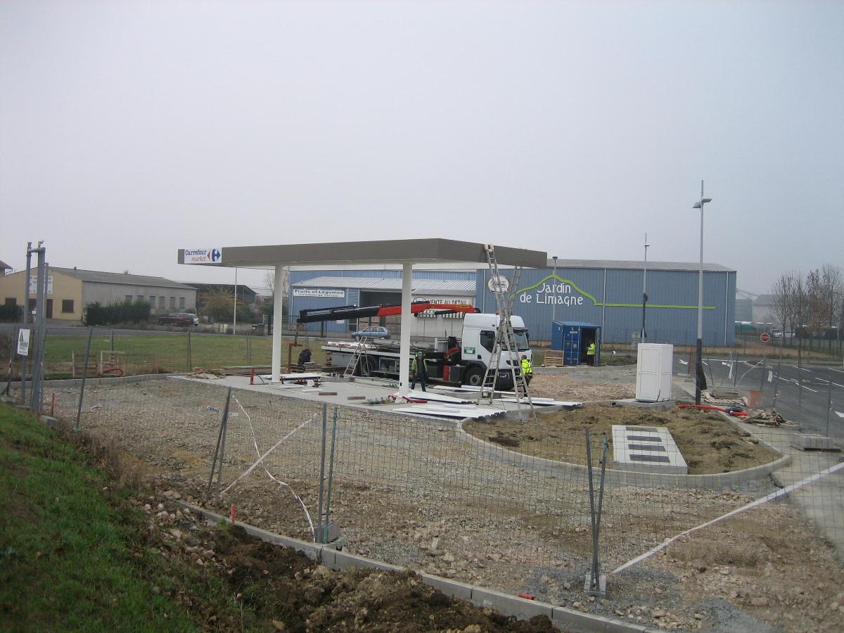 Station-service en construction, un camion est stationné sous l'auvent. Le bâtiment est entouré de gravier et de béton.