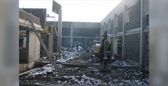 Chantier : une pelleteuse dégage les débris. Façade du bâtiment partiellement démolie, ambiance hivernale.