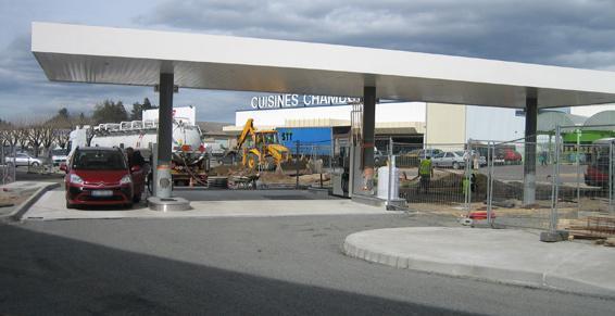 Voiture rouge dans une station-service en construction. Auvent et bâtiment en arrière-plan.