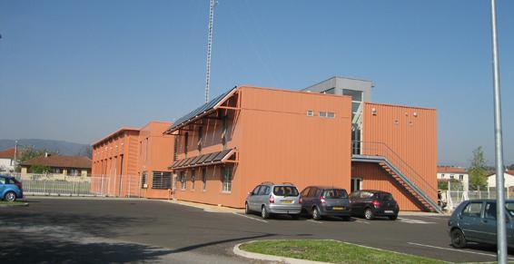 Bâtiment orange avec des voitures garées devant ; ciel bleu clair.