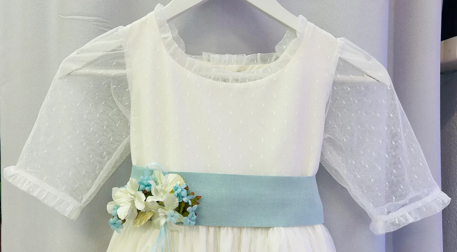 Un vestido blanco con una faja azul y flores cuelga de una percha.