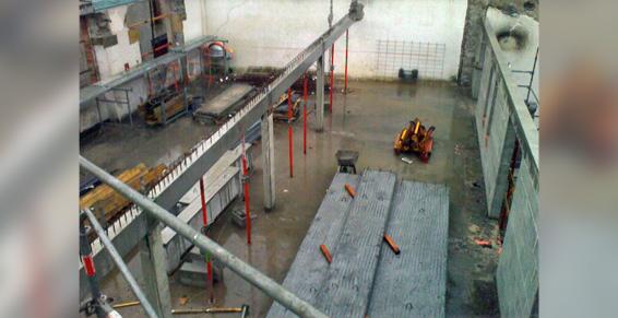 Intérieur du chantier, vue aérienne : dalles de béton, machines, poutres métalliques, sol inondé.