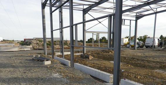 Charpente métallique d'un bâtiment en construction, métal gris, terre, fondation en béton.
