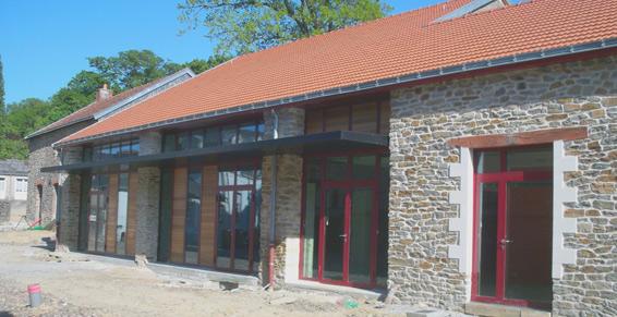 Bâtiment en pierre avec portes à cadre rouge et façade vitrée sous un toit en tuiles rouges.