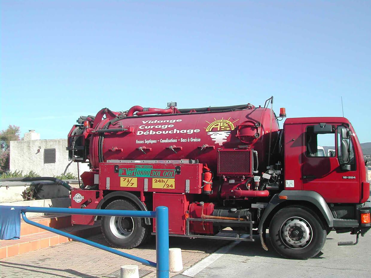 Camion aspirateur d'assainissement rouge garé à côté d'un bâtiment sous un ciel bleu clair