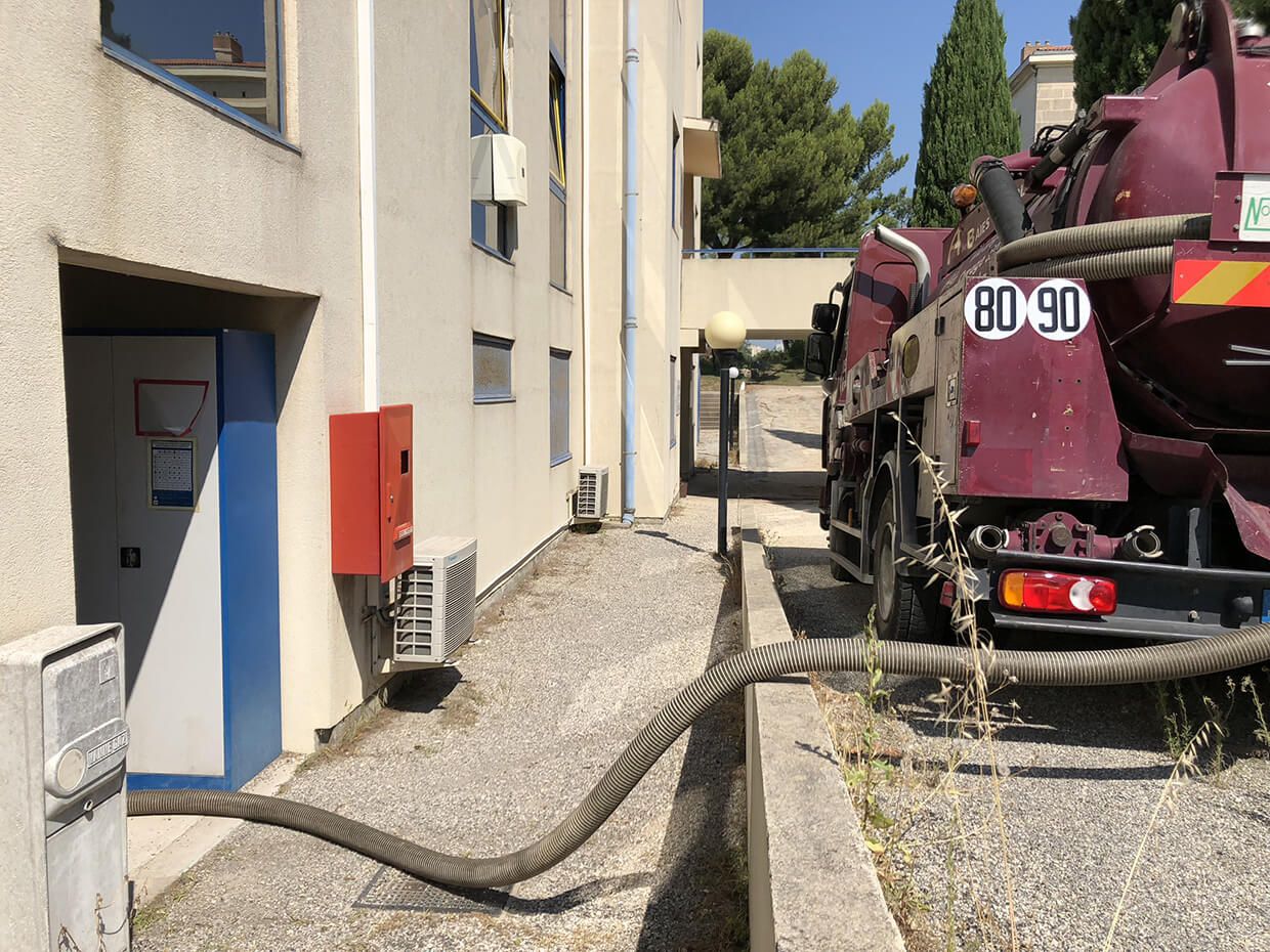 Camion de chantier avec tuyau d'arrosage dans une ruelle étroite à côté d'un bâtiment beige