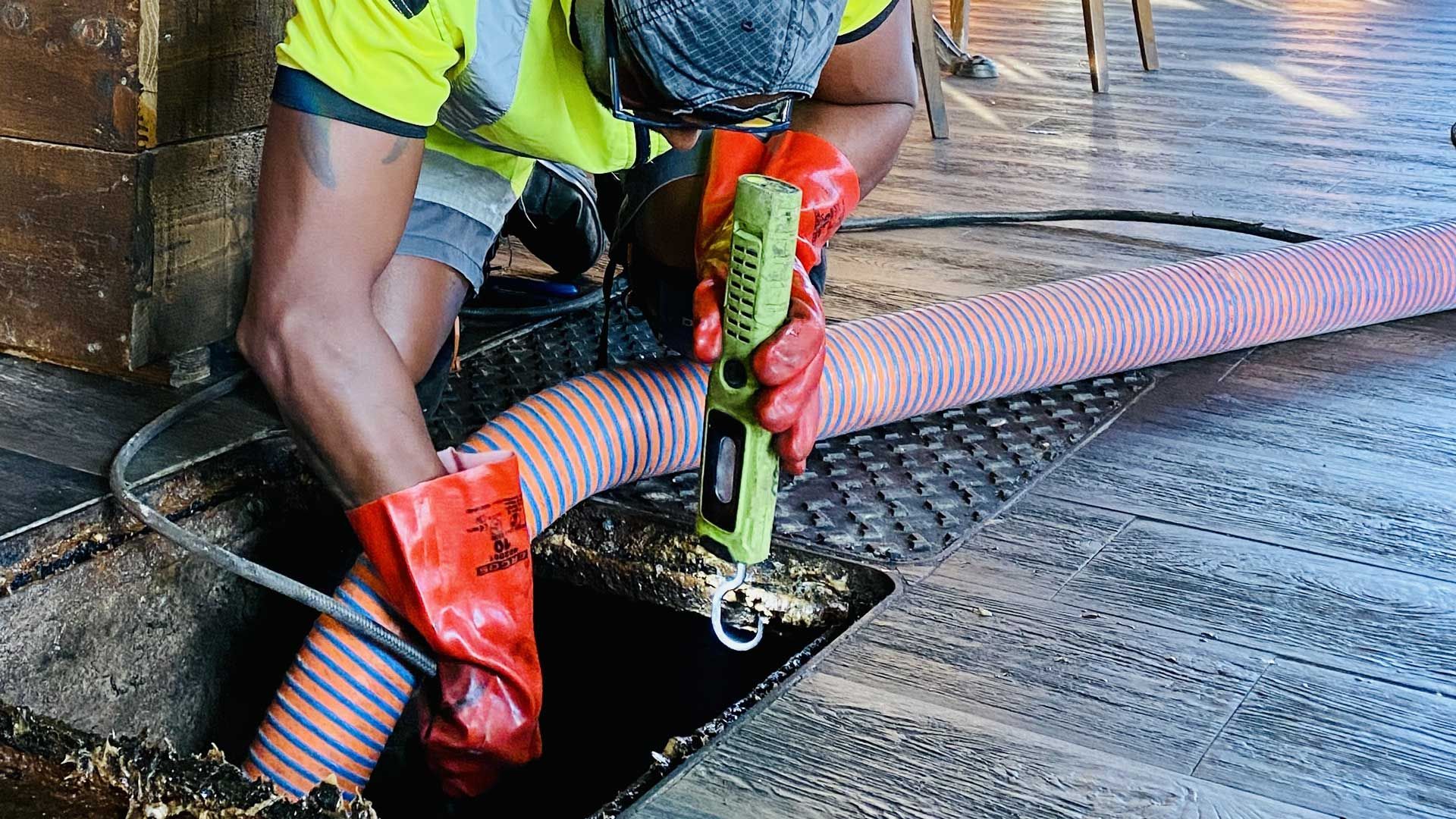 Un ouvrier en tenue de sécurité en train de déboucher une canalisation sous une grille en acier ouverte