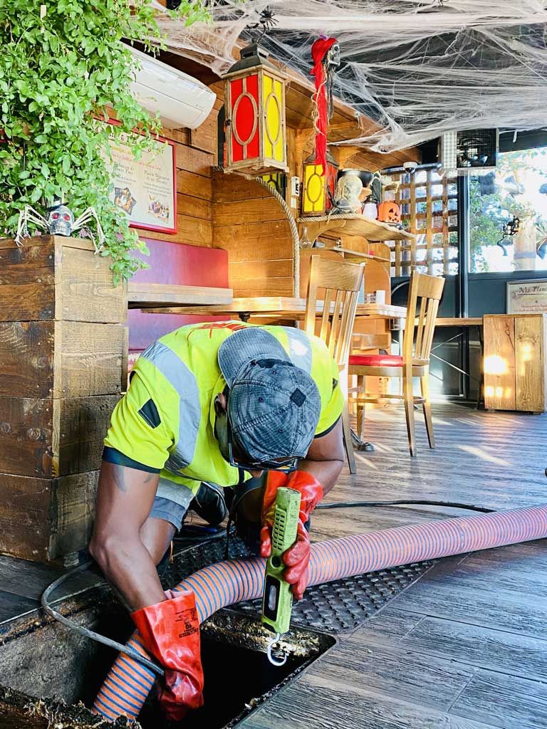 Un ouvrier en tenue de sécurité en train de déboucher une canalisation sous une grille en acier ouverte